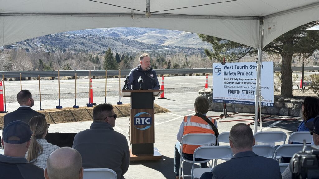Reno City Councilmember Devon Reese speaks at the podium during the West Fourth Street Safety Project groundbreaking ceremony on March 2, 2026. An RTC-branded lectern and project signage are visible, with ceremonial shovels and orange construction cones lined up along the corridor in the background.